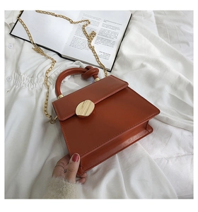 Detail of red-brown PU leather handbag with knot handle and gold chain on white fabric