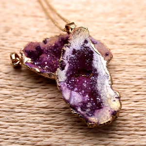 Primer plano del colgante de ágata druzy púrpura con borde dorado sobre fondo tejido