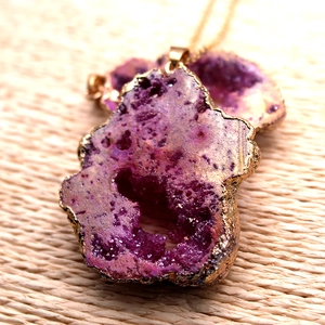 Primer plano de un colgante de ágata druzy púrpura natural con bordes dorados refinados