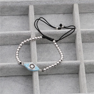 Handmade woven bracelet with silver beads and evil eye charm in a grey jewelry tray
