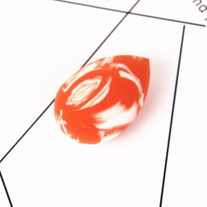 Detail eines tropfenförmigen Make-up-Schwamms mit orange-weißer Marmorierung und Poren