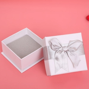 Opened white square gift box with silver ribbon and grey lining on pink background