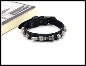 Close-up of black leather bracelet with metal bullets and rivets on white background