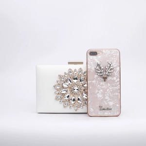 White satin rhinestone evening clutch bag shown next to a smartphone for size scale