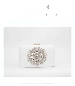 Close-up of white evening clutch with ornate floral crystal flower and gold metal clasp