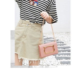 Detail of pink PU leather crossbody bag with golden cat-shaped metal clasp and chain strap