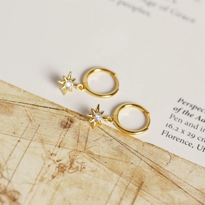 Detail of gold eight-pointed star hoop earrings with white zircon on vintage book background