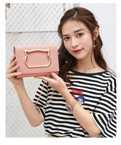 Pink crossbody bag detail showing cat-shaped golden clasp and chain held by a model