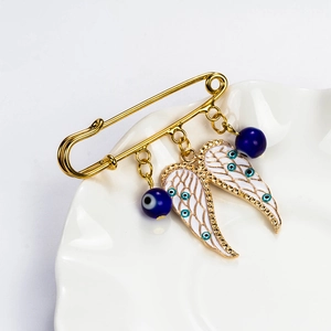 Detail of angel wing brooch with blue evil eye beads on a white ceramic plate