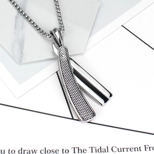 Macro shot of silver razor pendant with textured handle and box chain on grey background