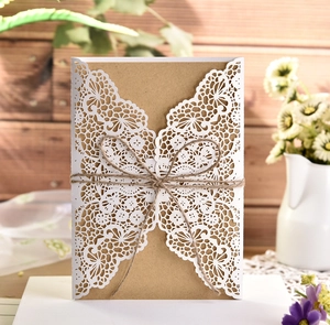 Close-up of laser-cut lace invitation card with natural twine bow on rustic wood