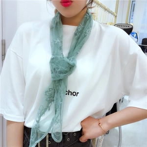 Detail view of a green lace scarf with floral embroidery tied in a stylish small bow knot