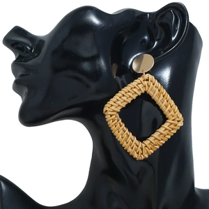 Détail de boucles d'oreilles bohèmes en rotin tressé avec clou doré et pendentif géométrique