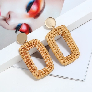 Détail de boucles d'oreilles géométriques en rotin tressé main avec clous dorés sur revue
