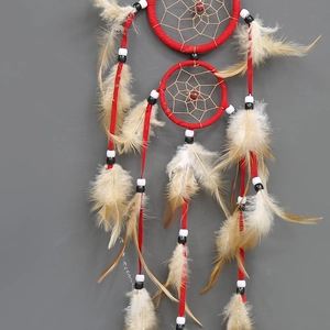 Red double hoop dreamcatcher with beige feathers and black beads on a grey wall