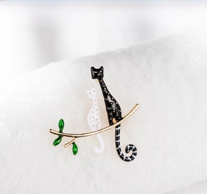 Dettaglio della spilla creativa con gatti in smalto bianco e nero su ramo dorato