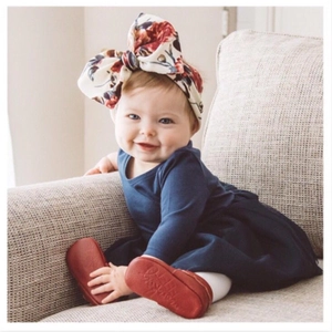 Baby girl wearing a floral print large bow headband with a dark blue long sleeve dress