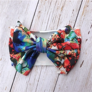 Detailed view of floral baby headband with large bow on a white wood texture background