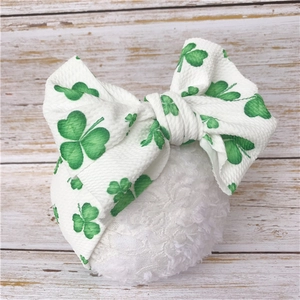 Detail of white knit baby headband with green clover print and large bow on wood