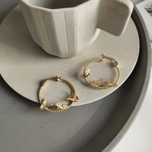 Detailed close-up of gold irregular butterfly earrings on white ceramic tray