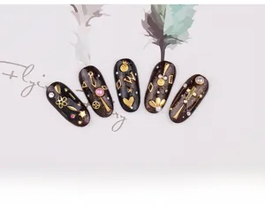 Close-up of assorted gold metal nail art charms with pearls on black nails