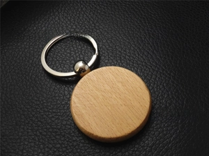 Close-up of a smooth round beech wood keychain on a black textured leather background