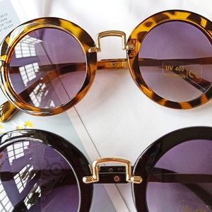 Detail of round kids sunglasses with leopard and black frames plus golden metal bridges