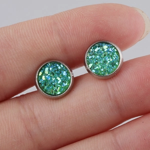 Macro shot of 8mm round blue-green druzy glitter stud earrings on a finger