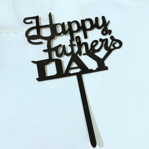 Detail view of a black acrylic Happy Father's Day cake topper on a white fabric background