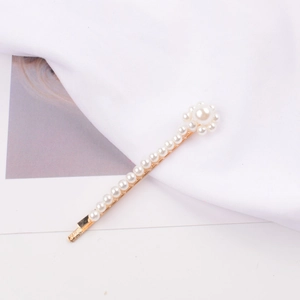 Close-up of golden hair clip with white pearls and flower detail on white fabric