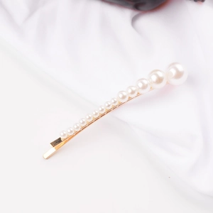 Detailed close-up of golden metal hair clip featuring gradient white faux pearls on white cloth