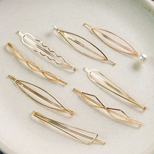8-piece set of gold geometric metal hair clips with pearls on a white ceramic plate