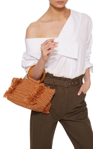 Detail of woven straw bag with round handles and tassel edges on a fashion model