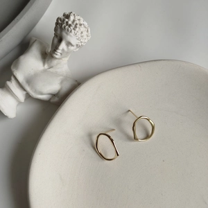 Detail of irregular hollow gold hoop earrings placed in a ceramic dish for display