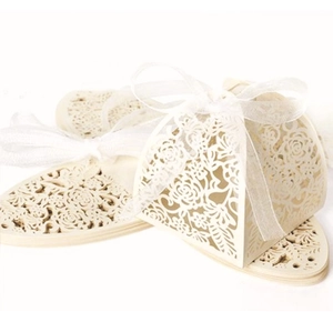 Detail of laser-cut beige favor box with rose patterns and white ribbon bow
