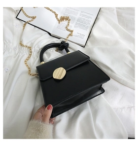 Detail of a black trapezoid handbag with gold chain strap on an aesthetic background