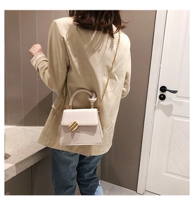 Detail of white handbag featuring a knotted handle and golden circular buckle on model