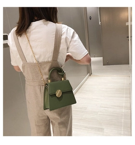 Close-up of green trapezoid crossbody bag featuring knot handle and gold chain strap