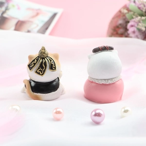 Detail von Miniatur-Katzenfiguren aus Harz in schwarz-goldenen und rosa Outfits auf Stoff
