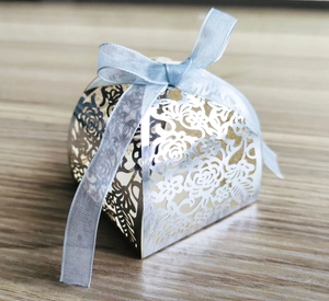 Close-up of silver laser-cut wedding favor box with floral patterns and a light blue ribbon