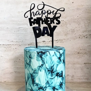Detail of black Happy Father's Day acrylic cake topper on blue marble textured cake