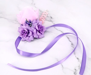 Detail of elegant purple silk roses wrist corsage with ribbons on marble background