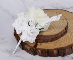 Close-up of white silk wedding corsage with roses on a rustic wood slice background