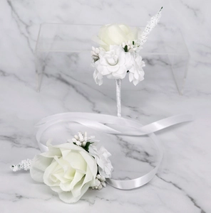 Macro view of white silk rose boutonniere and wrist corsage set for wedding ceremonies