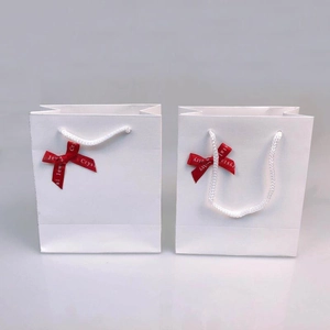 Detailed view of two white paper gift bags with red crystal jewelry ribbons and rope handles