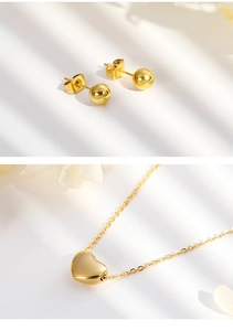 Detail of minimalist golden bead earrings and heart pendant necklace set on white surface