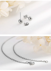 Detailed view of silver heart pendant necklace and ball stud earrings on white floral background