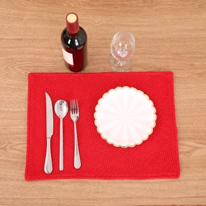 Red rectangular woven Christmas placemat with metallic cutlery on wooden background