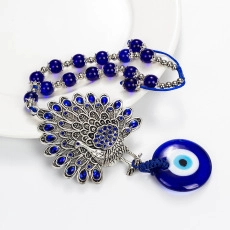 Close-up of a silver peacock pendant with blue beads and a glass Evil Eye charm