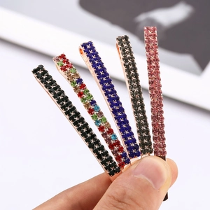 Macro detail of hand holding five colorful rhinestone bobby pins with alloy base